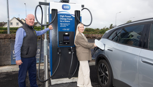 Man and woman standing by EV charging infrastructure with the woman charging a grey vehicle