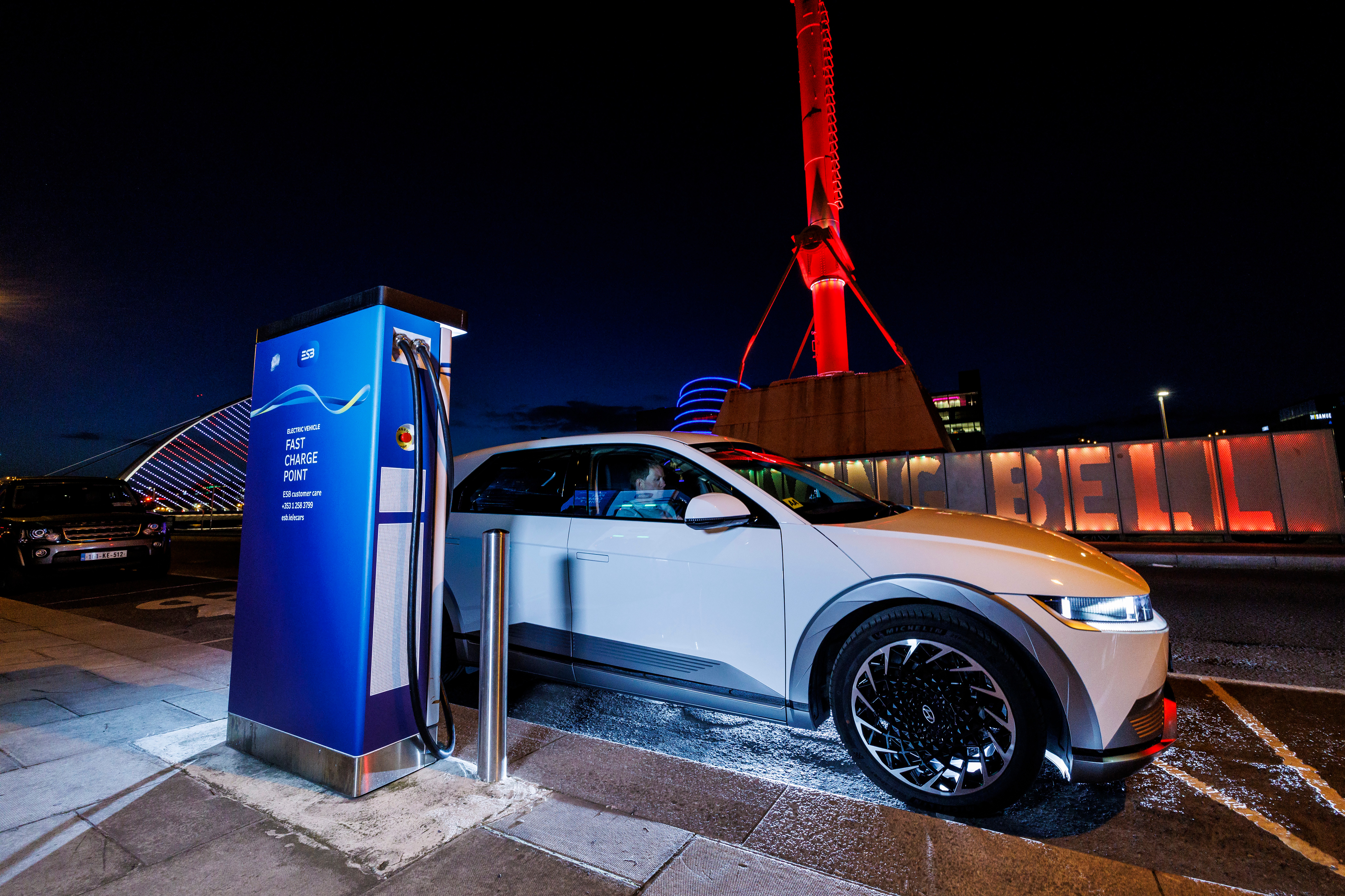 Photograph of a car standing at an ESB EV charging point on a city street at night