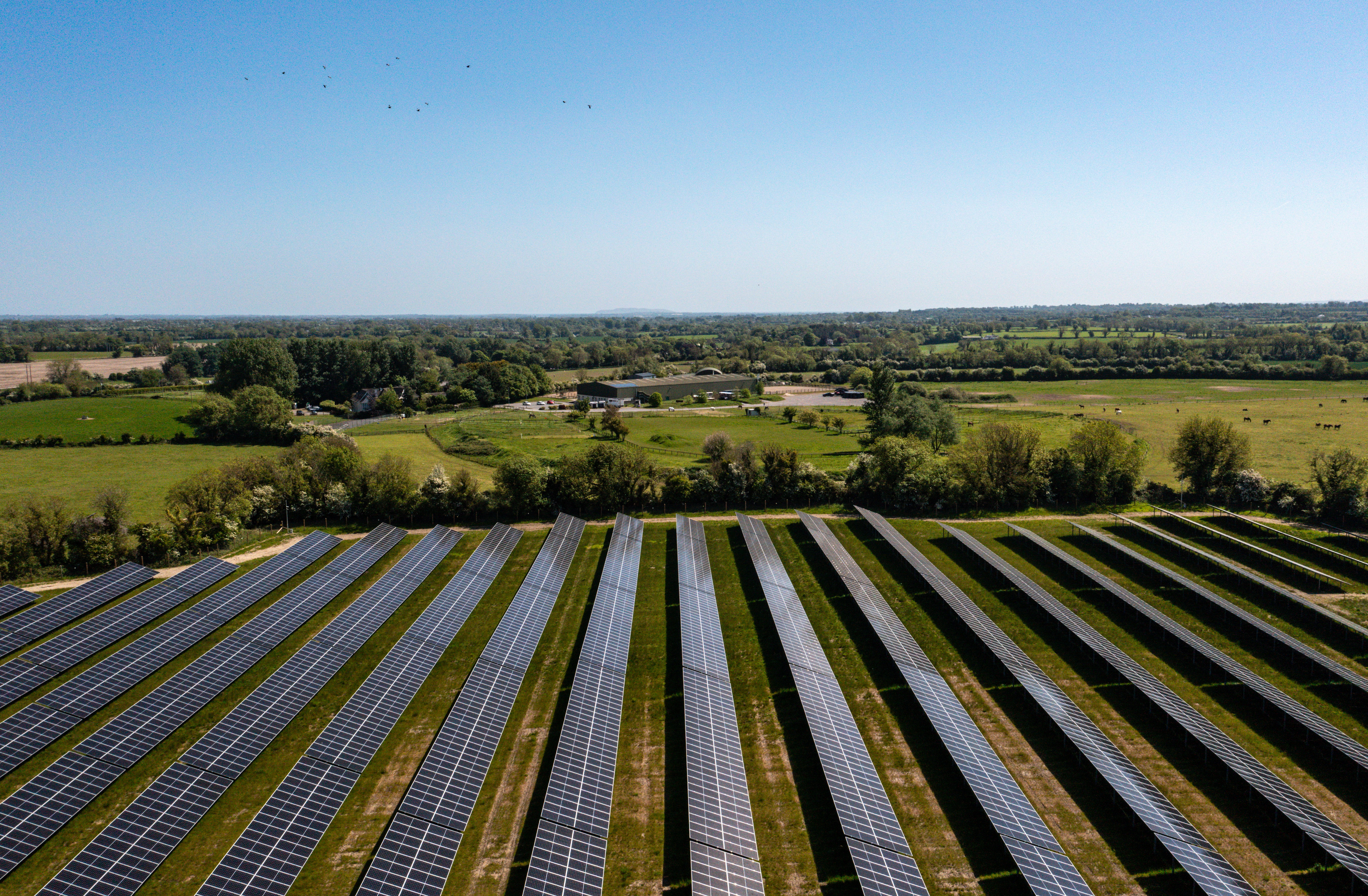 Photograph of rows of solar panels on a solar farm site surrounded by green fields 