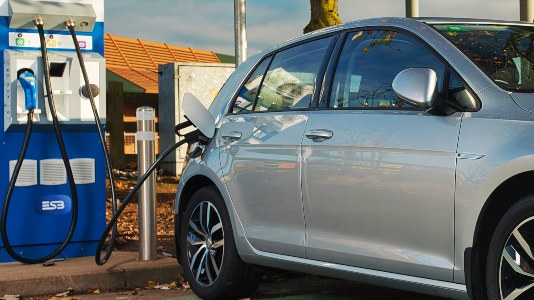 A grey car parked at an electric vehicle charge point with a cable insterted.