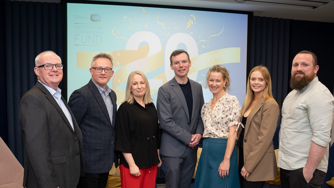 Group of seven people standing at an event in front of a screen with the number 20 on it
