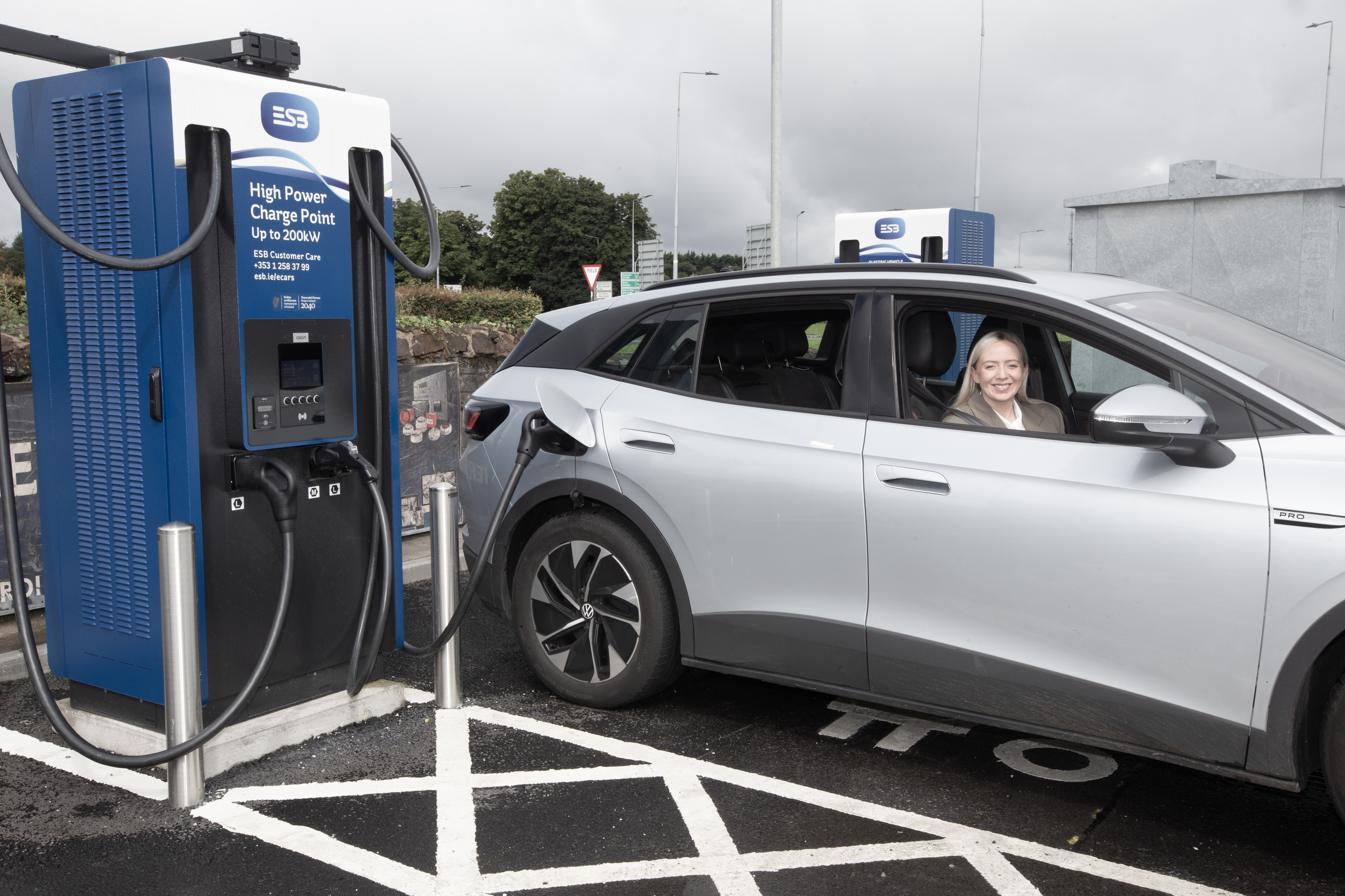 Photograph of high power ESB charger in a car park with electric car plugged in and smiling driver