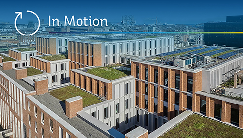 Photograph of a modern city skyline with green grassy roofs and overlaid text 'In Motion'