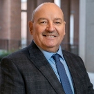 Owen Kilmurray, white man with no hair and wearing a black checkered shirt, blue shirt and navy tie