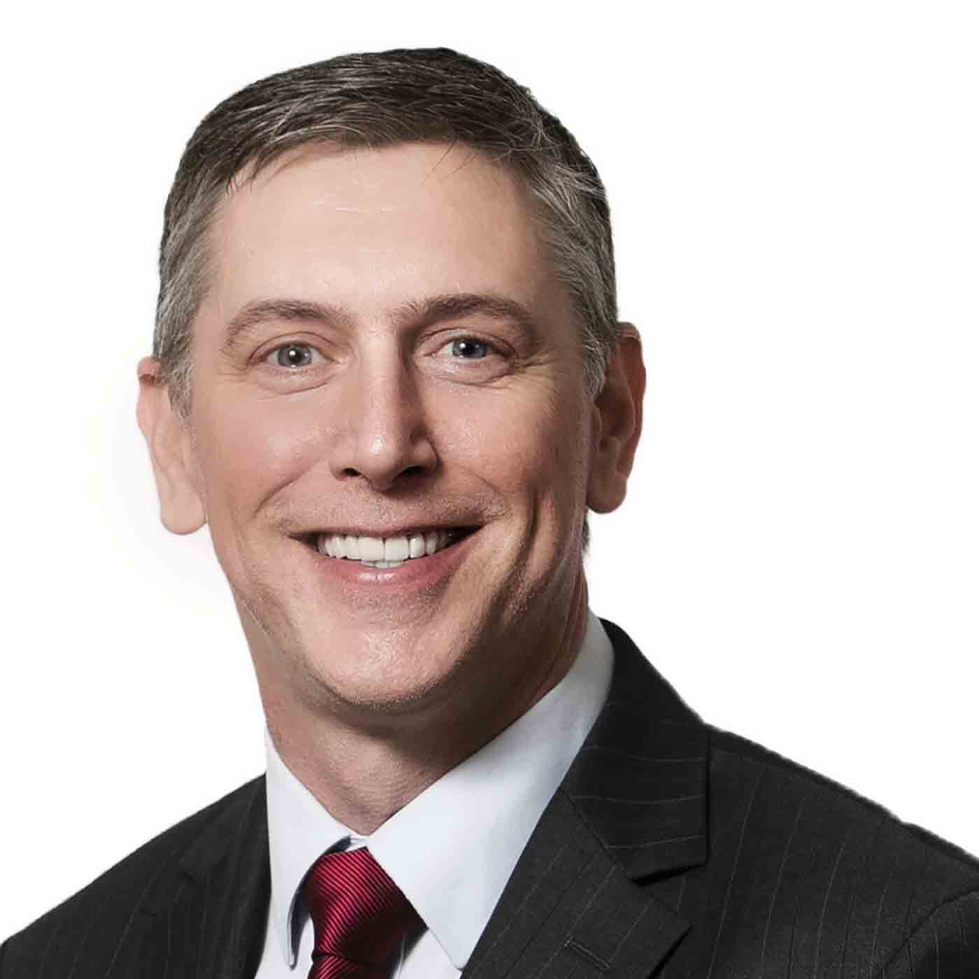 Paul Smith, white man with black/grey hair wearing a black suit, white shirt and red tie