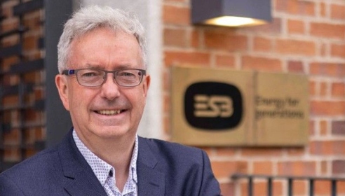 Photograph of a man in business attire standing in front of a building with the ESB logo