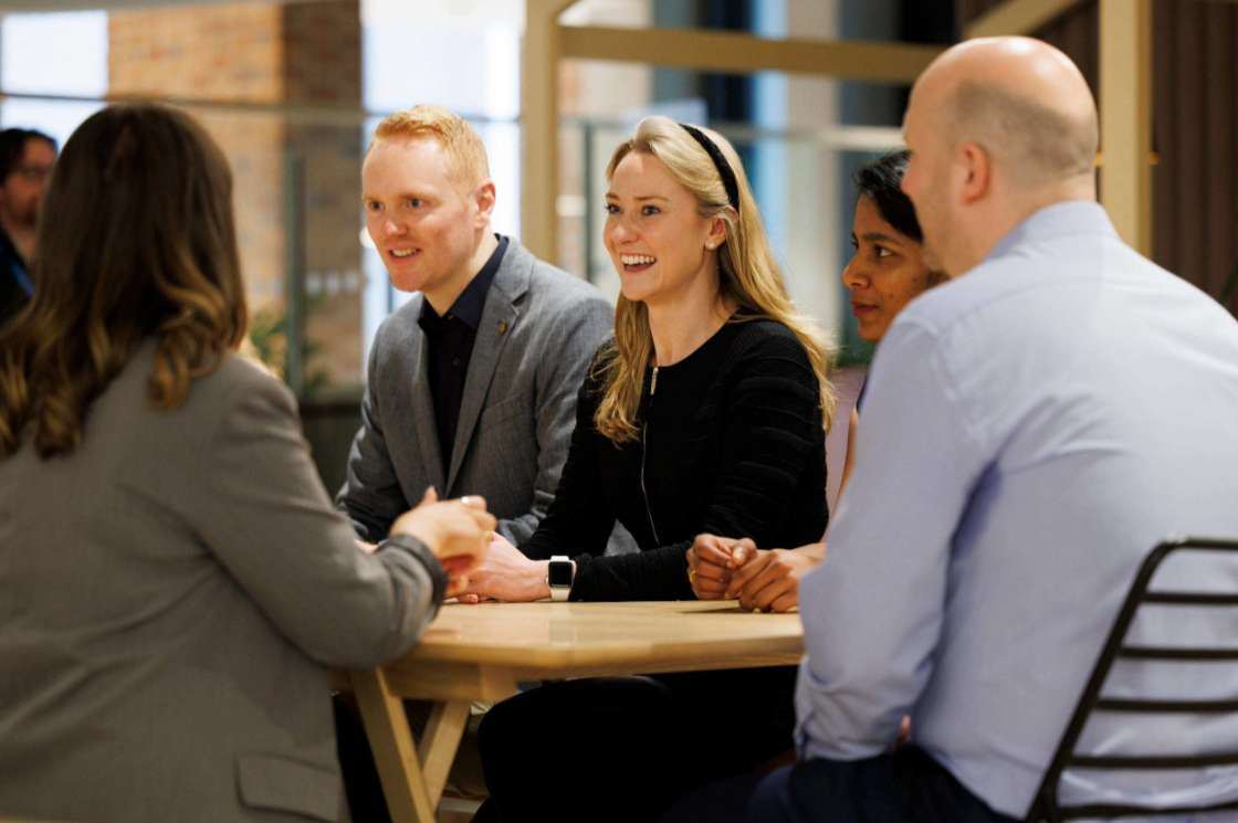 Team members gathered around a table during a workplace meeting in a modern office.