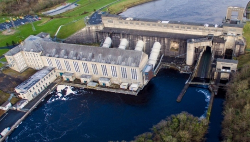 A large hydro electric generating station with two buildings and turbines surrounded by water and trees