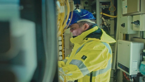 Image of a man wearing high vis and protective clothing working in a Telecommunications cabin.