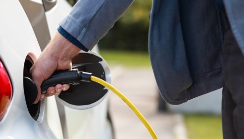 Person's hand putting an EV charger into a white car