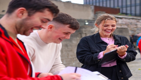 Three ESB graduates standing in a yard with one holding a notebook and pen