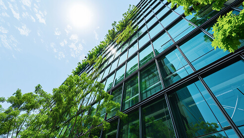 A grey office building with windows and green shrubbery to the front of it