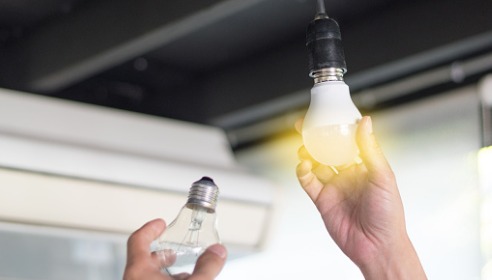 Man holding a turned on light bulb in one hand and a switched off one in the other hand.