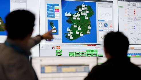 Two people standing and pointing to screens which has a map of Ireland and windmills on the map