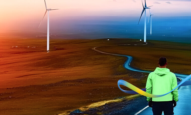 Man with yellow jacket walking along country road surrounded by onshore wind farm, mountains and brown rugged landscape