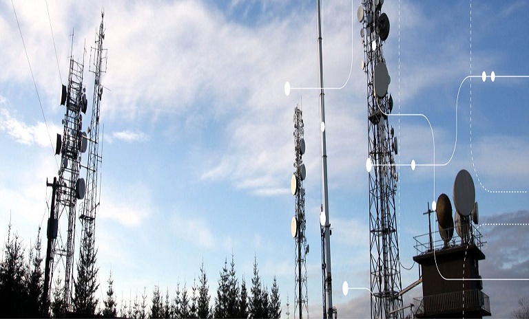Four Telecommunications Towers are pictured against the sky with trees also in the background