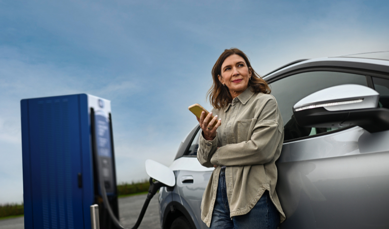 Woman standing by electric vehicle with mobile phone in her hand