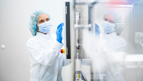 Woman with white coat, blue hat and gloves at a large machine