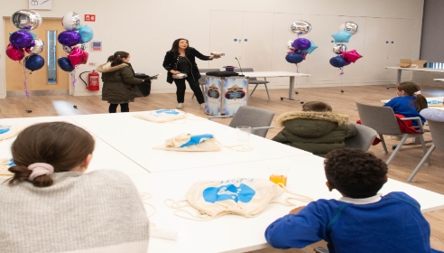 Woman with black clothes in room with children sitting and one standing with balloons in background