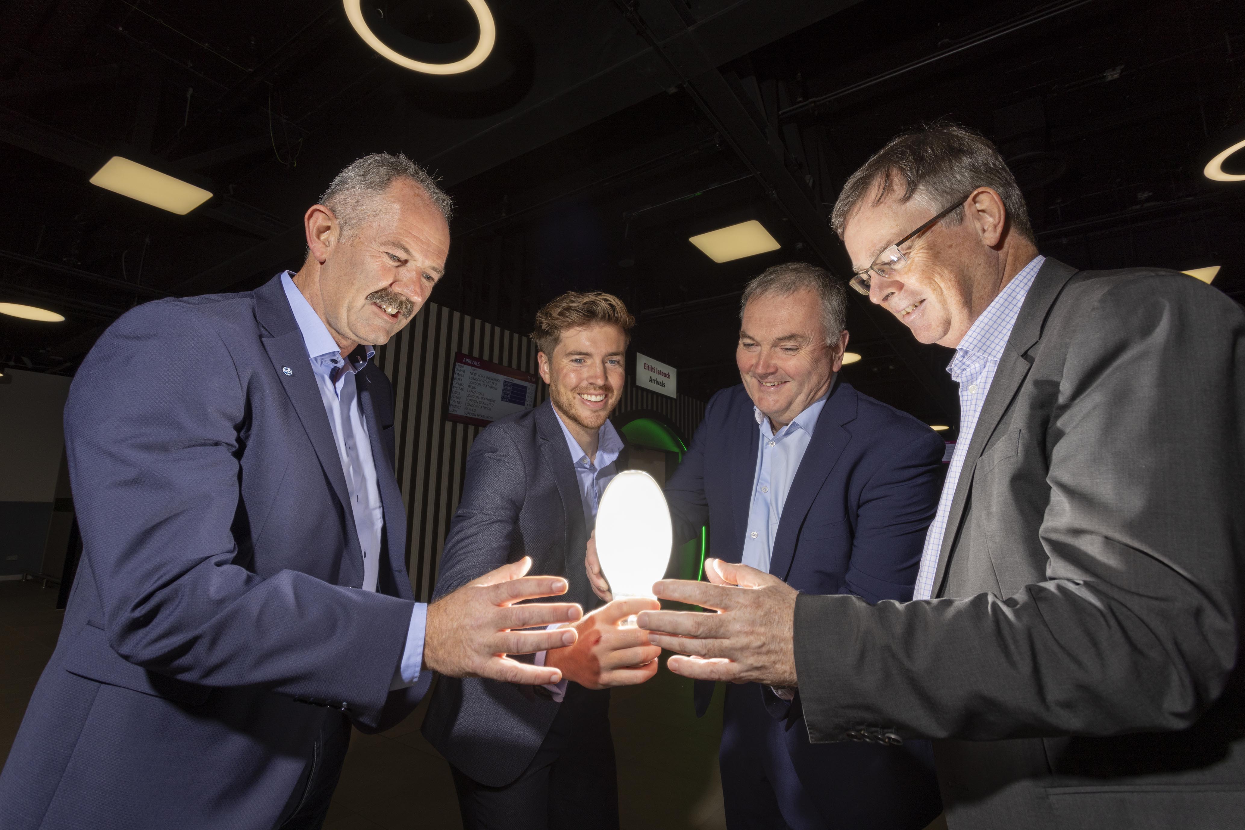 Four men dressed in suits all holding a lightbulb.