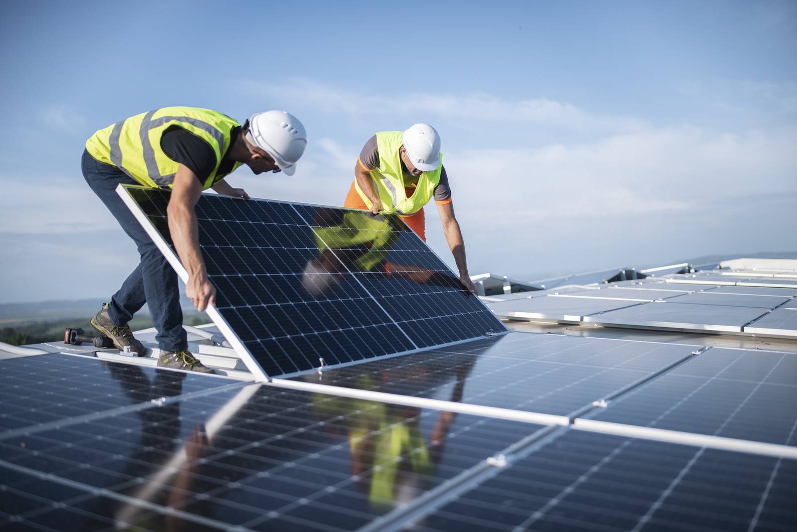 Two men in workwear installing solar panels on a roof