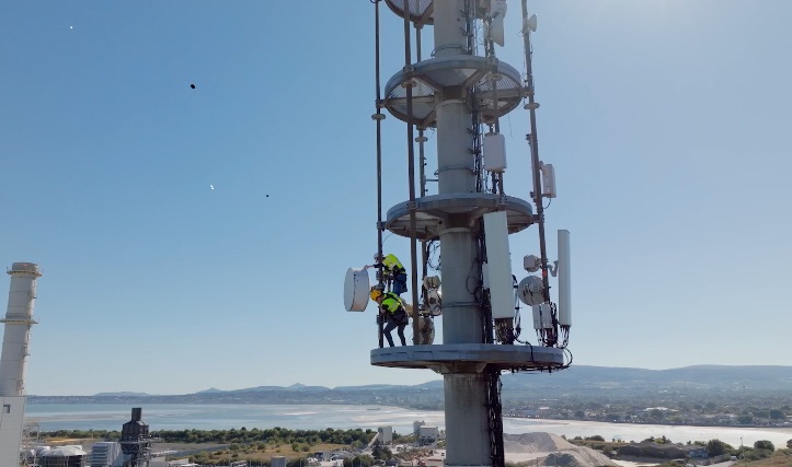 Rigger in high vis and protective clothing working on a telecommunications tower platform in Ringsend with Dublin Bay and city scape in the background, representing infrastructure maintenance and connectivity solutions.