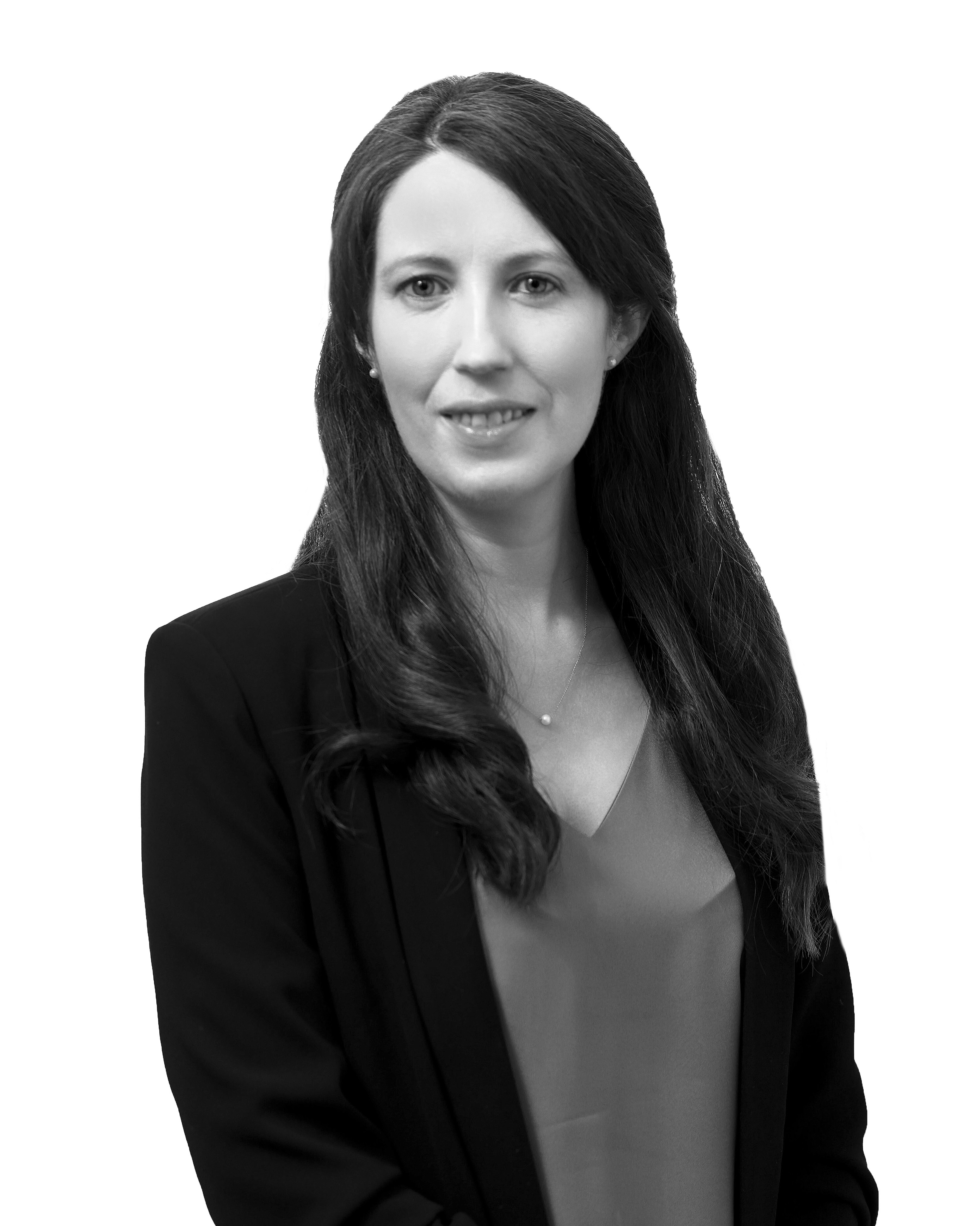 Black and white picture of a woman with long black hair wearing a black blazer, grey top and a necklace.