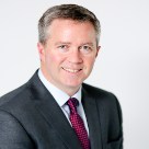 Paul Stapleton, white man with black/grey hair wearing a black suit, white shirt and wine coloured tie