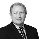 Black and white picture of a man with grey hair and wearing a black jacket, white shirt and stripey tie