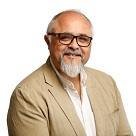 Image of man wearing a beige jacket and white shirt and glasses with a beard.