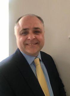 Man with brown skin wearing a navy jacket, blue shirt and yellow tie.