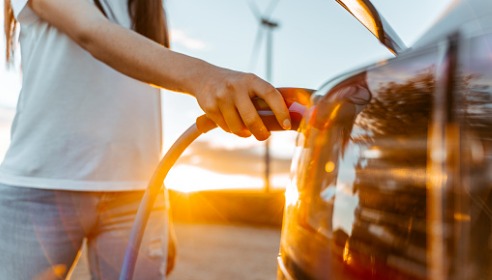 Woman holding electric vehicle charger as it plugs into car with a wind turrbine in the background