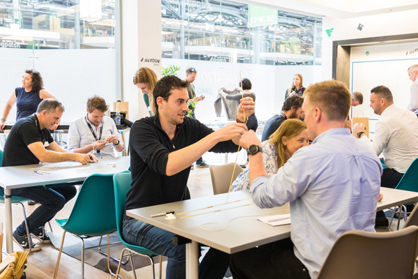 People sitting in an office space on chairs solving problems with straws and lines. 