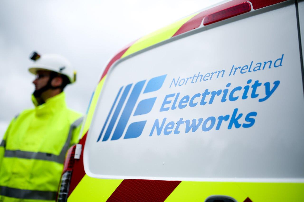 Man with a yellow high vis jacket and hard hat standing beside a van that says Northern Ireland Electricity Networks